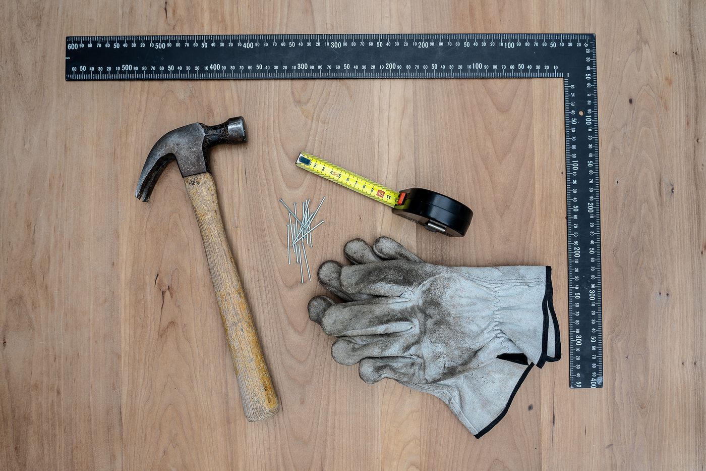 Hammer, tape measure, framing square and work gloves laid out on a wood floor