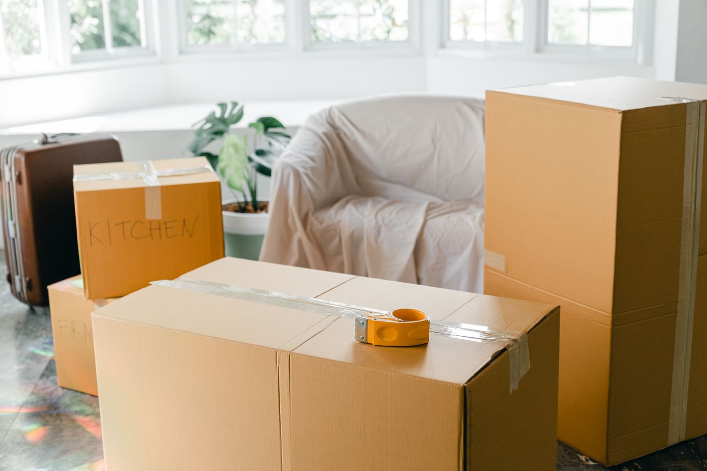 Packed moving boxes and furniture under dust sheets in an empty room