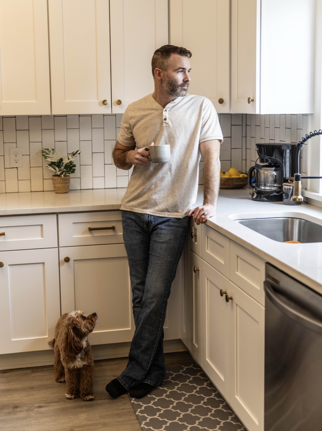 Wade Bartels leaning on the kitchen counter with a cup of coffee, dog at his feet