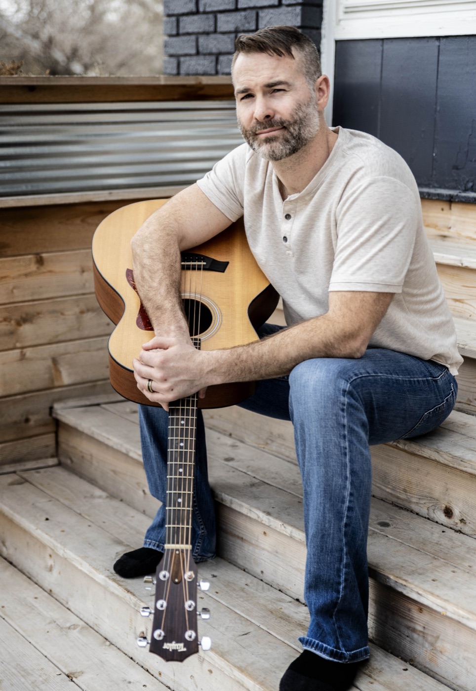 Wade Bartels sitting on porch steps with an acoustic guitar