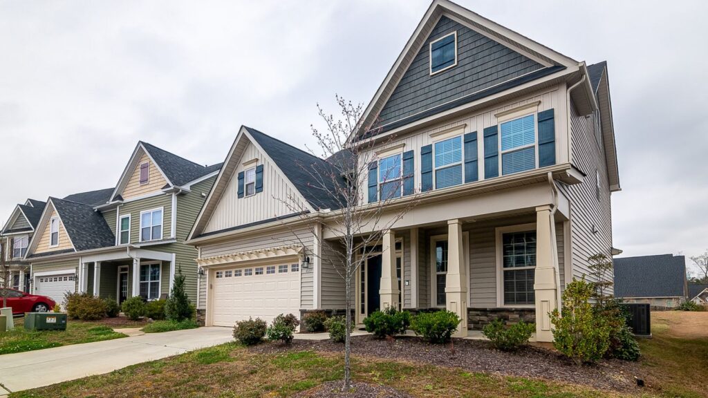 A row of modern suburban homes with garages, driveways, and landscaped lawns in daylight.