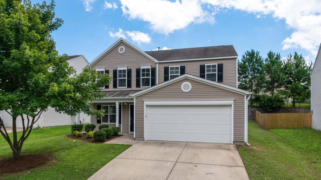 Charming two-story suburban home with green lawn, two-car garage, and blue sky.