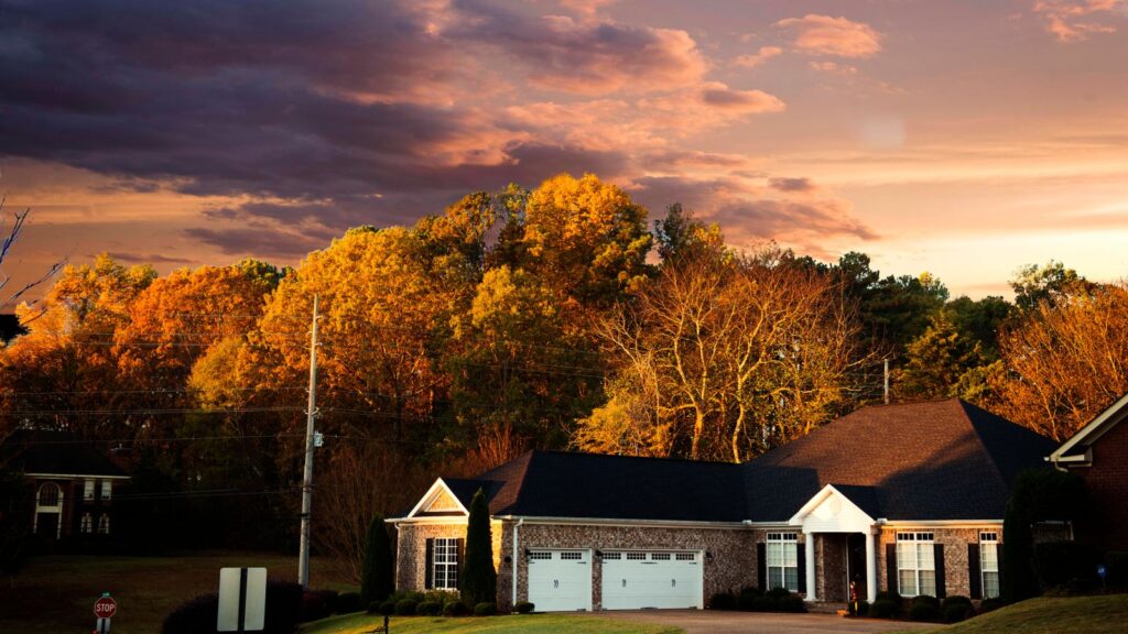 A picturesque suburban house surrounded by fall foliage under a dramatic sunset sky in Madison, AL.