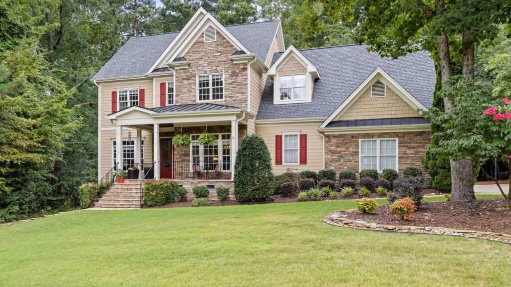 Two-story house surrounded by lush greenery and well-maintained lawn.