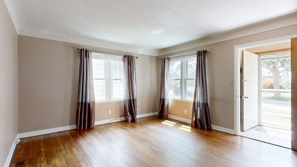 Spacious and well-lit empty living room with hardwood floors and open door.